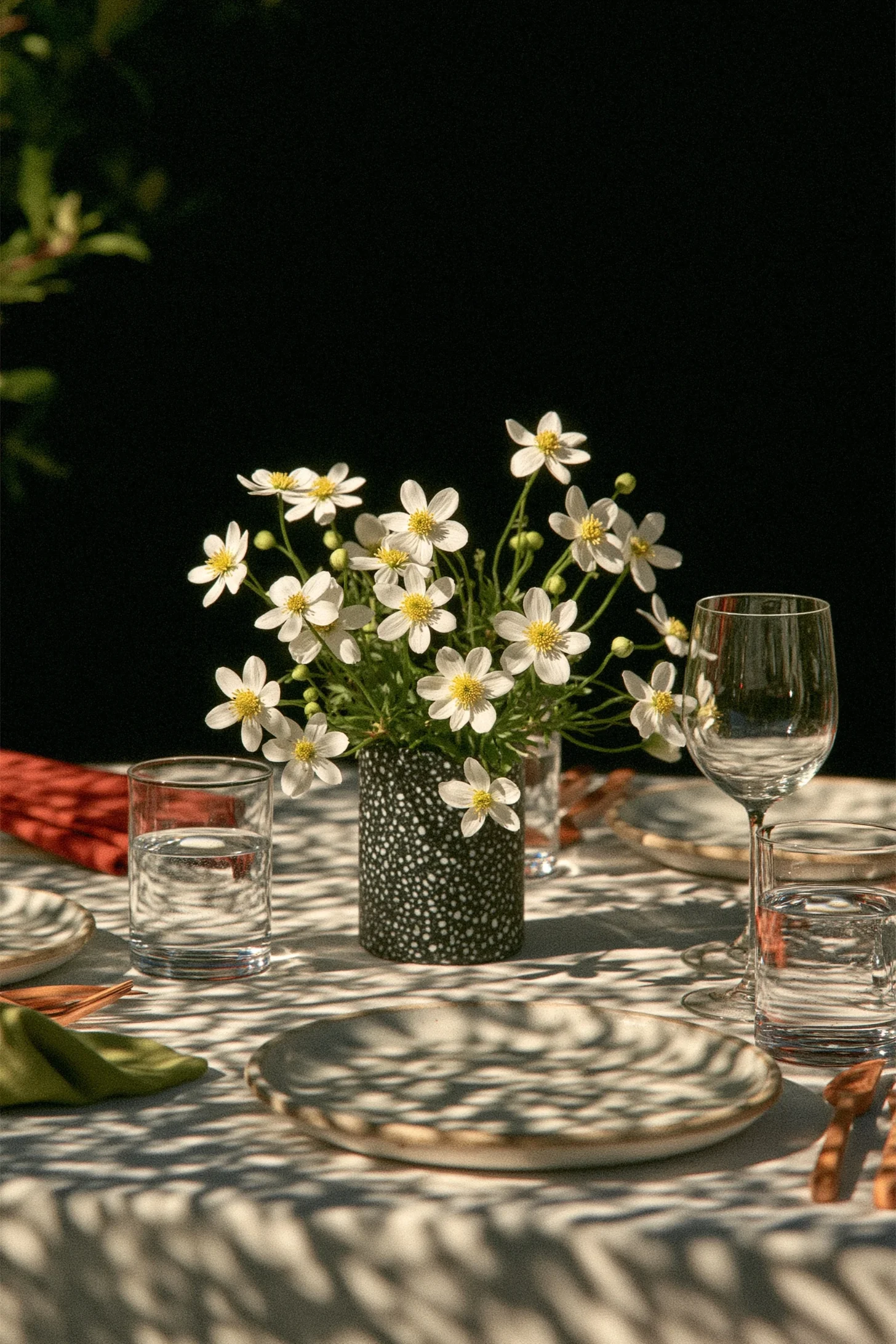 A moody green wedding tablescape with a fern and white daisy centerpiece, layered linens and candlelight