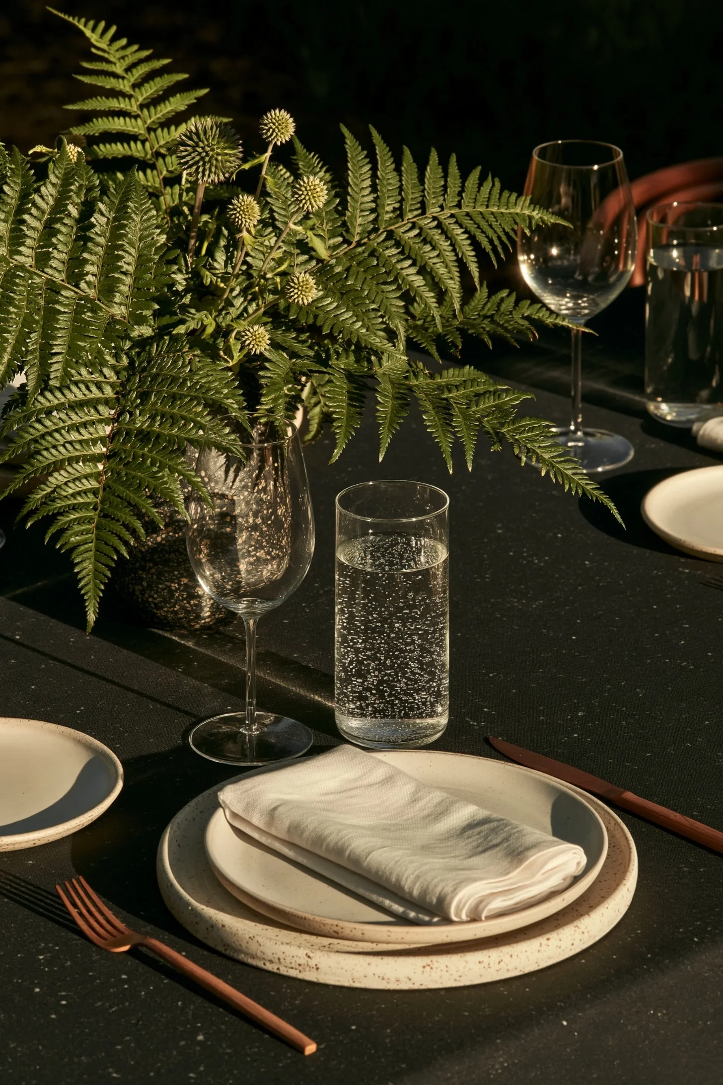 A dark green wedding place setting with a low fern centerpiece, white daisies and warm candlelight